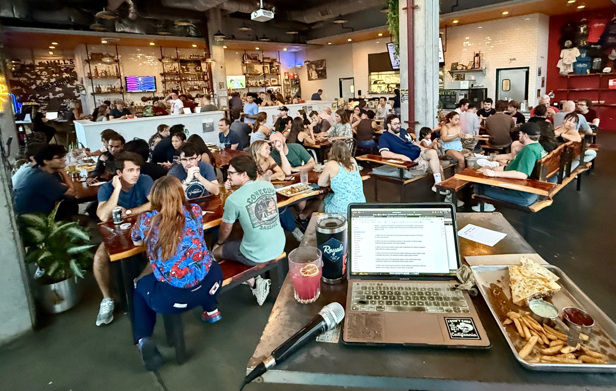 A packed Industry Trivia night in East Austin, viewed from the host table with microphone and laptop in the foreground